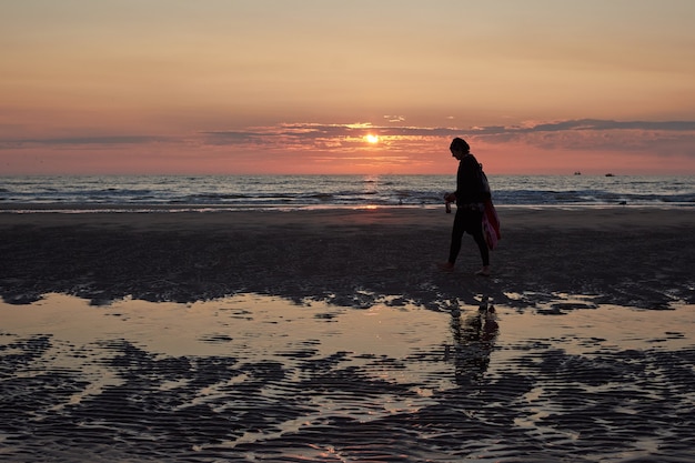 Widok z tyłu kobiety spacerującej po plaży podziwiającej malowniczy zachód słońca
