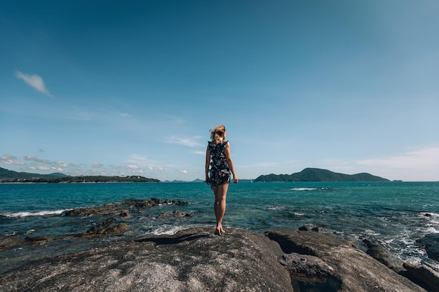 Widok z tyłu kobiety stojącej przed morzem. Widok z tyłu młoda dziewczyna na skałach w pobliżu dzikiego oceanu