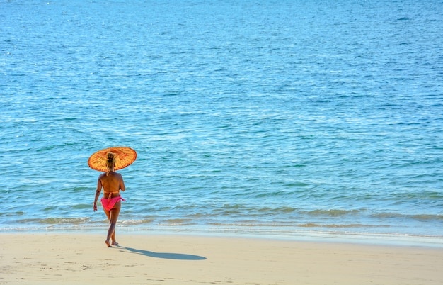 widok z tyłu kobiety w kolorowe bikini spaceru na plaży z parasolem