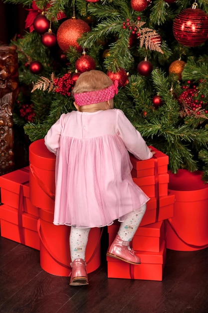Widok z tyłu mała dziewczynka ubrana w różową sukienkę na choinkę ozdobioną tłem w domu w pomieszczeniu