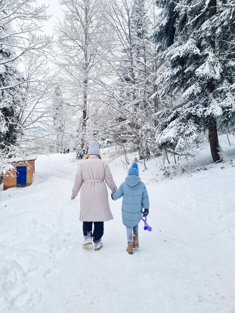 Widok z tyłu matka i córka spacerują po zaśnieżonym lesie lub parku