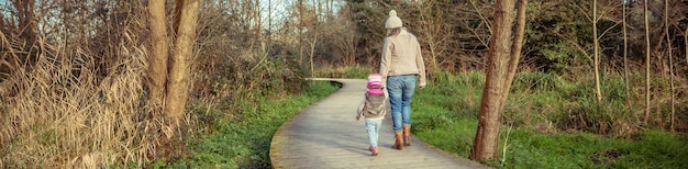 Widok Z Tyłu Matki I Córki Idących Razem Trzymających Się Za Ręce Nad Drewnianą ścieżką Do Lasu