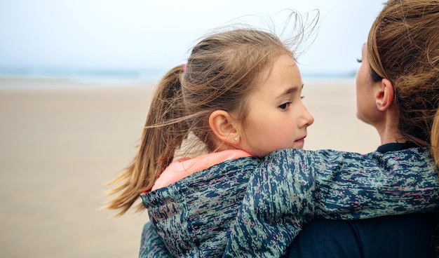 Widok z tyłu matki i córki patrzących na morze na plaży jesienią