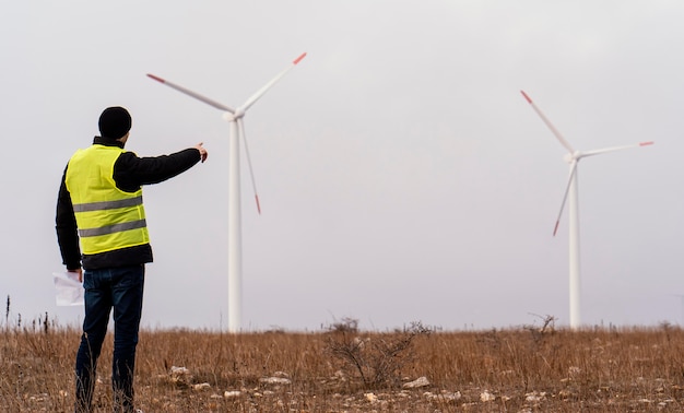 Zdjęcie widok z tyłu męskiego inżyniera patrząc na turbiny wiatrowe w tej dziedzinie