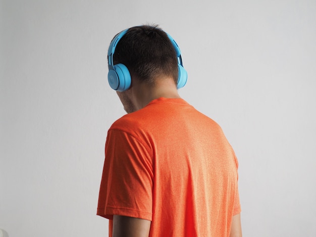 Zdjęcie widok z tyłu mężczyzny noszącego niebieskie bezprzewodowe słuchawki i pomarańczowy t-shirt, słuchający muzyki.