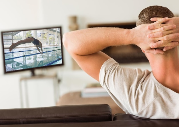 Widok z tyłu mężczyzny siedzącego na kanapie oglądając kanał sportowy w telewizji w salonie