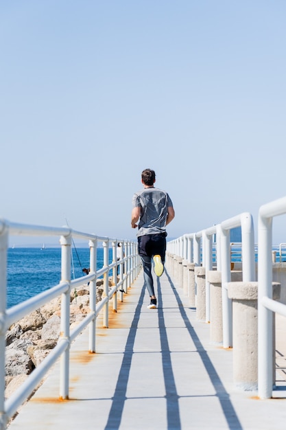 Zdjęcie widok z tyłu młodego mężczyzny biegnącego wzdłuż promenady w pobliżu morza?