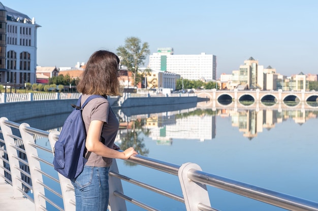 Widok z tyłu młodego studenta z kręconymi włosami stojącego w parku na tle rzeki