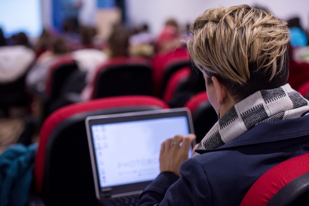 widok z tyłu młodej bizneswoman piszącej na klawiaturze laptopa podczas seminarium w sali konferencyjnej