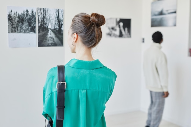 Widok z tyłu młodej kobiety ubranej na zielono, patrząc na sztukę w przestrzeni kopii galerii lub muzeum