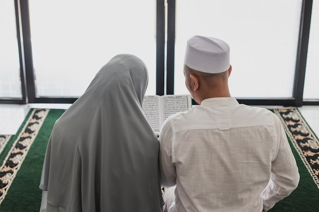 Widok z tyłu muzułmańskiej pary czytającej Koran lub Koran razem w meczecie