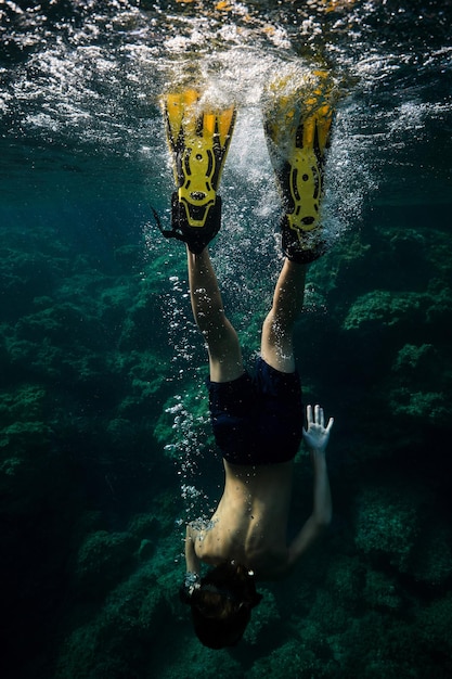 Widok z tyłu na całe ciało anonimowego nurka w kombinezonie i płetwach nurkujących pod przezroczystą wodą morską z rafami koralowymi na dnie
