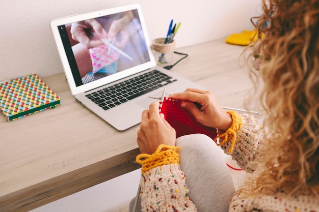 Widok z tyłu na kobietę w domu podążającą za kanałem samouczka na laptopie, aby nauczyć się robić na drutach