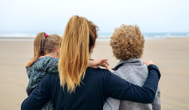 Zdjęcie widok z tyłu na trzy pokolenia kobiet patrzących na morze na plaży jesienią