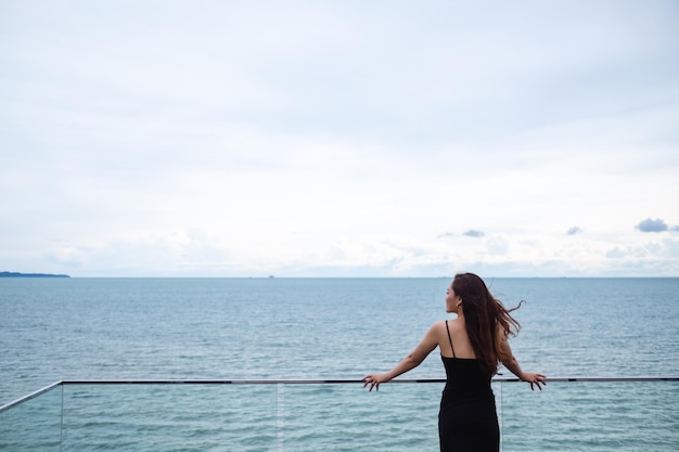 Widok z tyłu obrazu pięknej młodej azjatyckiej kobiety stojącej i patrzącej na morze i błękitne niebo