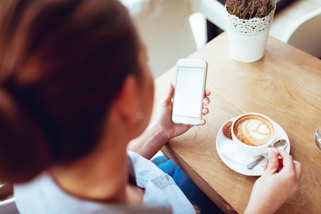 Widok z tyłu piękna młoda uśmiechnięta biznesowa kobieta za pomocą inteligentnego telefonu w kawiarni.