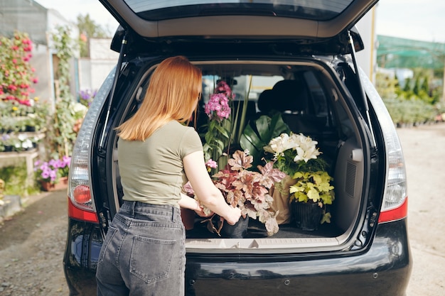 Widok Z Tyłu Rudowłosej Kobiety W Koszulce I Dżinsach Stojącej Przy Otwartym Bagażniku I ładującej Kwiaty Do Samochodu Po Zakupach Na Targu Kwiatowym