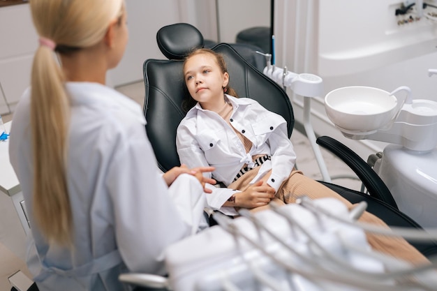 Widok z tyłu słodkiej dziewczynki siedzącej na krześle dentystycznym i skarżącej się na ból odwiedzającej dentystę pediatrycznego Zapobieganie i profilaktyka chorób zębów