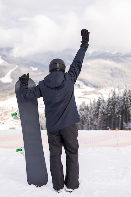 Zdjęcie widok z tyłu sportowca ze snowboardem, oglądając naturę ręką do góry