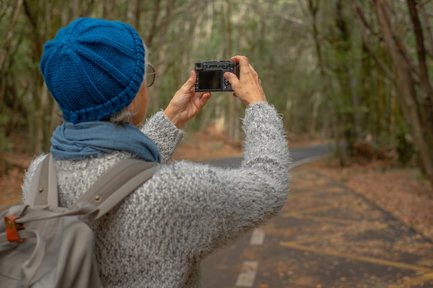 Widok z tyłu starszej kobiety fotografa turysty podczas wycieczki na świeżym powietrzu w lesie cieszącej się wolnością