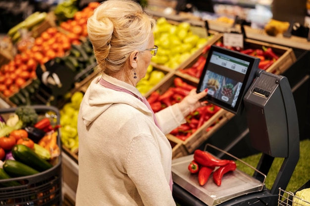 Widok z tyłu starszej kobiety mierzącej warzywa na wadze w supermarkecie