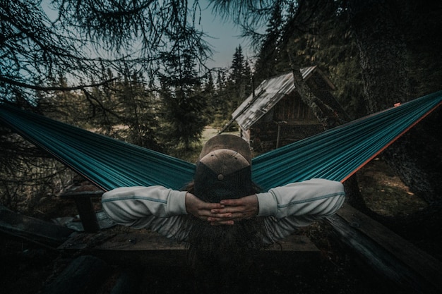 Widok z tyłu sylwetki człowieka relaksującej się na niebieskim hamaku między drzewami, ciesząc się widokiem i cichym krajobrazem gór Mglisty las
