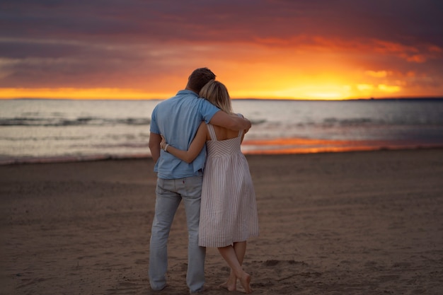 widok z tyłu szczęśliwej pary przytulającej się na plaży o zachodzie słońca