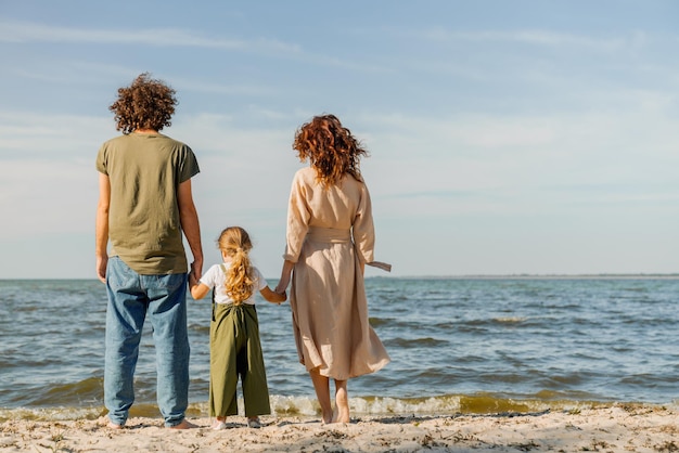 Widok z tyłu szczęśliwej rodziny stojącej i patrzącej na ocean, będąc na plaży