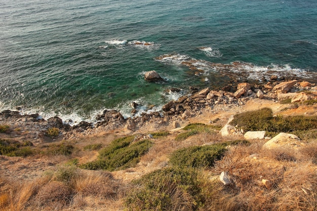 Widok ze stromego brzegu morza wzgórza pokrytego trawą, skałami i błękitną wodą oceanu w tle. Karpass, Cypr Północny