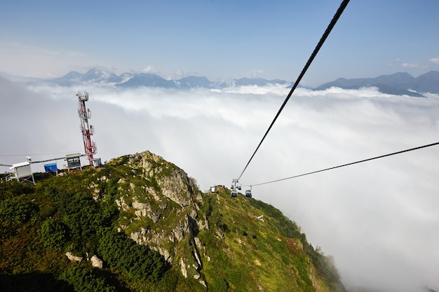 Widok ze szczytu kolejki linowej z wieloma miejscami siedzącymi i rozciągniętymi kablami nad drzewami w głębokiej mgle. Góry Kaukazu Północnego.