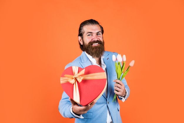 Zdjęcie wieczny prezent na wiosnę prawdziwy dżentelmen z bukietem koncepcji daty miłosnej brodaty mężczyzna w formalnej odzieży z kwiatami tulipanów i pudełkiem elegancki biznesmen nosi elegancką odzież na formalne wydarzenie