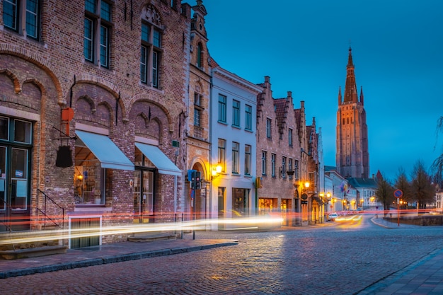 Wieczór na ulicach Brugii po deszczu. Widok nocy Onze Lieve. Vrouw Brugge na tle niebieskiego wieczornego nieba. Belgia.