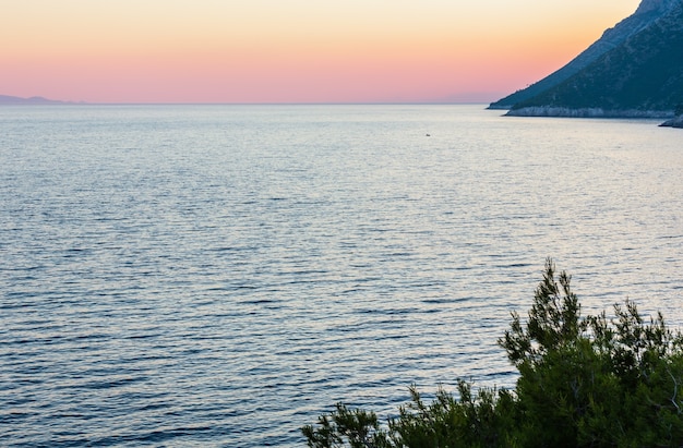 Wieczorny letni widok na wybrzeże z różowym zachodem słońca i lśniącą powierzchnią wody (Ston, półwysep Peljesac, Chorwacja)
