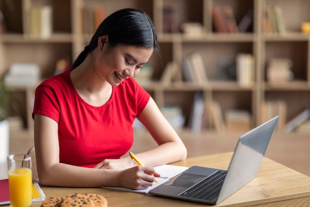 Wiedza i praca domowa Uśmiechnięta młoda azjatycka studentka z laptopem ogląda lekcję online