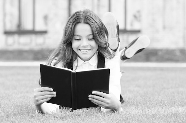 Wiedza to więcej niż informacja Szczęśliwa mała dziewczynka czyta książkę na zielonej trawie Urocza mała uczennica zdobywa wiedzę z czytania Dzień wiedzy lub 1 września Sprawdź swoją wiedzę szkolną