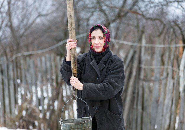 Wiejska kobieta z wiadrem zbiera wodę od studni