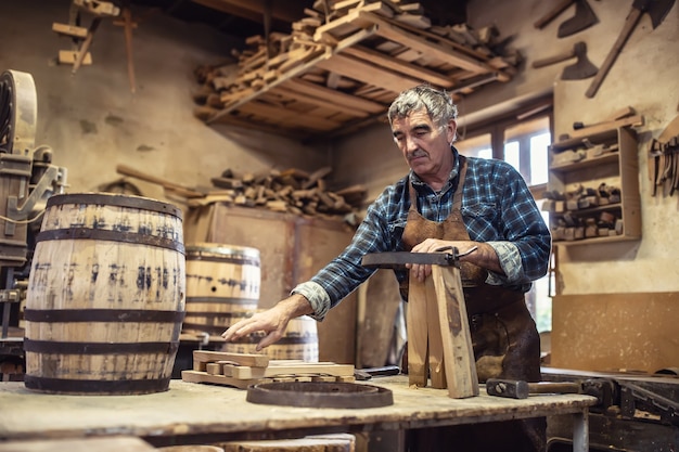 Wiekowy rzemieślnik buduje drewniane beczki w swoim warsztacie vintage.