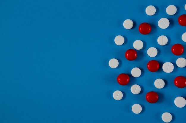 Wiele białych i czerwonych tabletek na niebieskim tle