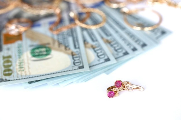 Wiele drogich złotych pierścionków z biżuterią, kolczyków i naszyjników z dużą ilością banknotów dolarowych na białym tle Lombard lub sklep z biżuterią