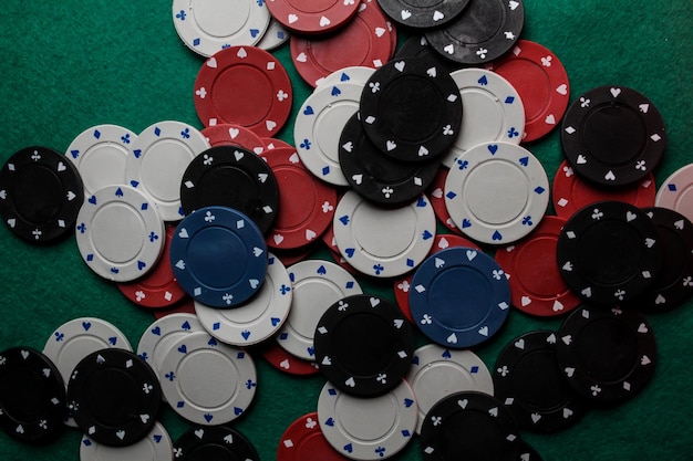 Wiele kolorowych żetonów do gry w kasynie leży na zielonym aksamitnym stole do gry. Tło dla hazardu.