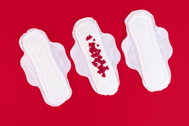 Wiele Małych Czerwonych Serduszek, Symboli Cyklu Miesiączkowego, Na Kobiecej Podpasce. Produkty Do Higieny Kobiecej Podczas Cyklu Menstruacyjnego. Czerwone Tło. Skopiuj Miejsce. Zdjęcie Wysokiej Jakości