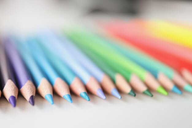 Wiele ostrych wielokolorowych ołówków leżących nad kolorami tęczowego tła zbliżenia