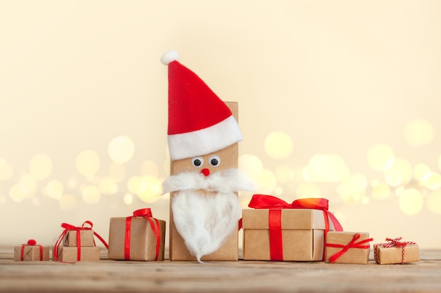 Wiele ręcznie robionych pudełek świątecznych owiniętych w papier prezentowy rzemieślniczy ozdobiony Santa Hat na drewnianym tle z musującym bokeh. Koncepcja nowego roku, świąt i uroczystości