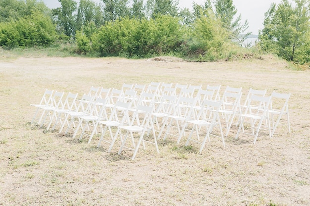 Zdjęcie wiele rzędów białych drewnianych krzeseł na ceremonię ślubną w przyrodzie