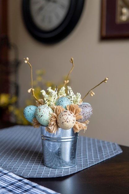Wielkanocna kompozycja z kolorowymi jajkami na stole. Metalowe wiaderko z bukietem pisanek