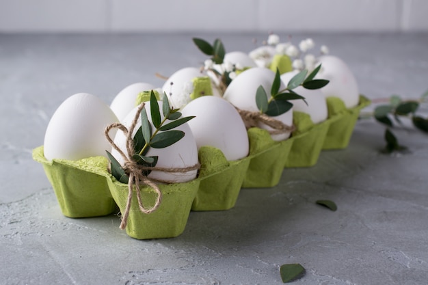 Wielkanocna wiosenna kompozycja dekoracyjna z białymi surowymi jajkami kurczaka w zielonym kartonowym pudełku Ozdobiona liśćmi eukaliptusa