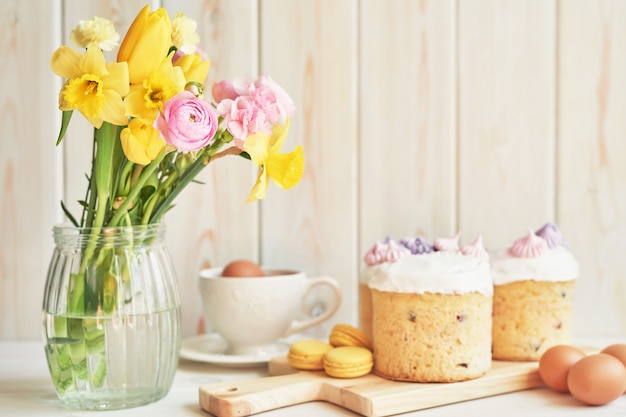 Wielkanocne ciasta na stole, makaroniki, jajka i bukiet kwiatów w wazonie