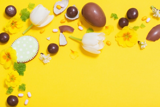Wielkanocne żółte tło z czekoladowymi jajkami cukierkami i wiosennymi kwiatami