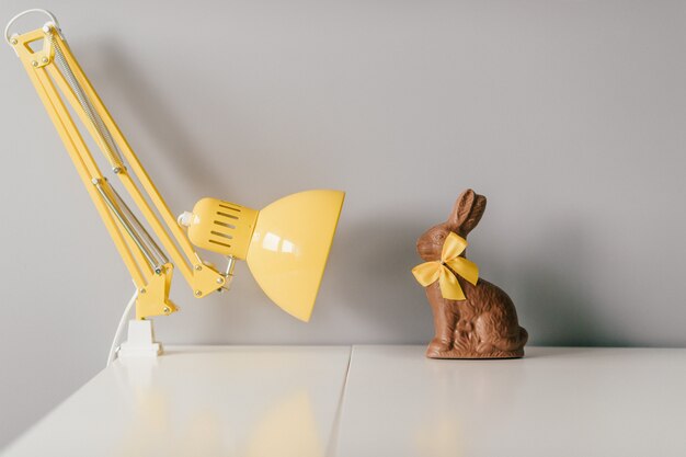 Wielkanocny czekoladowy królik z żółtym bowtie siedzi na stole z lampą