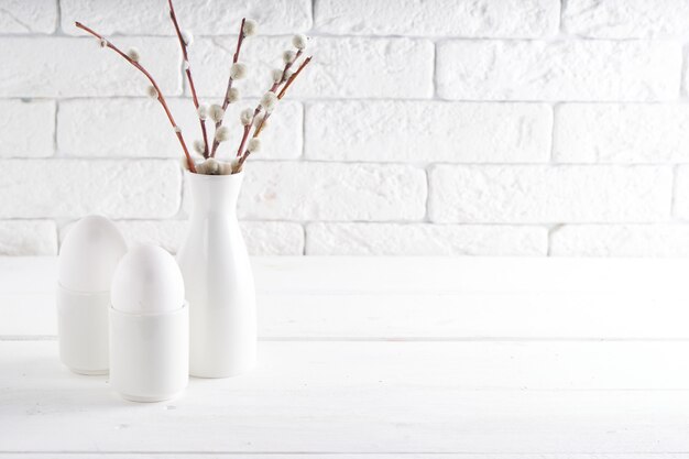 Wielkanocny pojęcie Biała waza z wierzby gałąź i filiżankami na białym stole Kopiuje przestrzeń